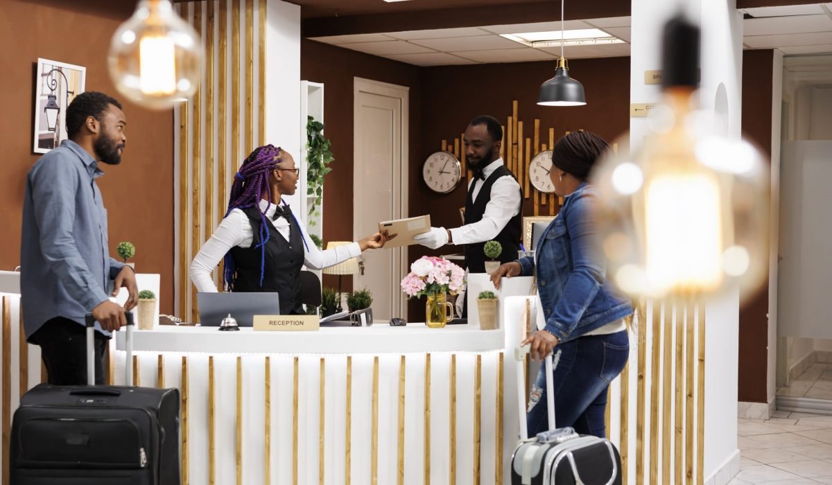 African American couple man an woman standing at hotel reception checking in at reception, waiting for room key or access card. Front desk staff managing guest check-in or check-out process